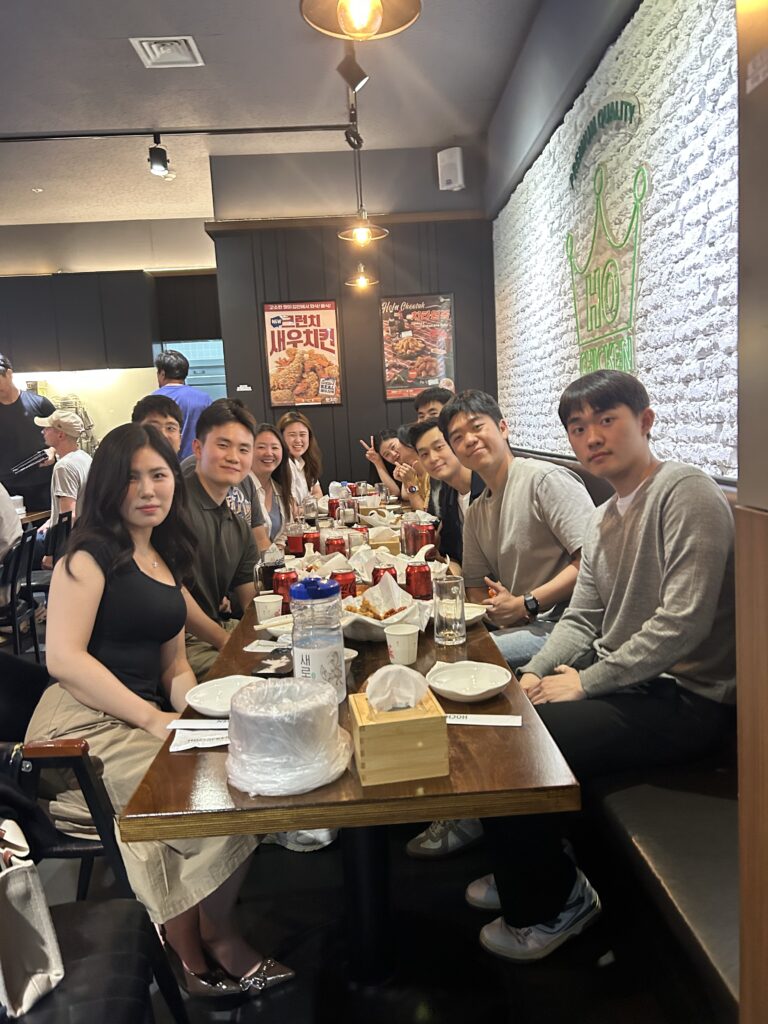 Participants seated together at a long table during NEXT-A Networking Night in Pyeongtaek, sharing chicken and conversation in a casual group setting.